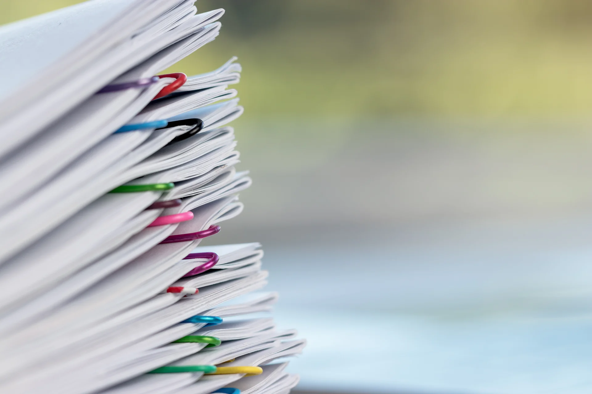 Eine Nahaufnahme von mehreren Papierstapeln, die mit bunten Büroklammern zusammengehalten werden. Die Papiere sind ordentlich gestapelt und die Büroklammern heben sich durch ihre leuchtenden Farben ab.