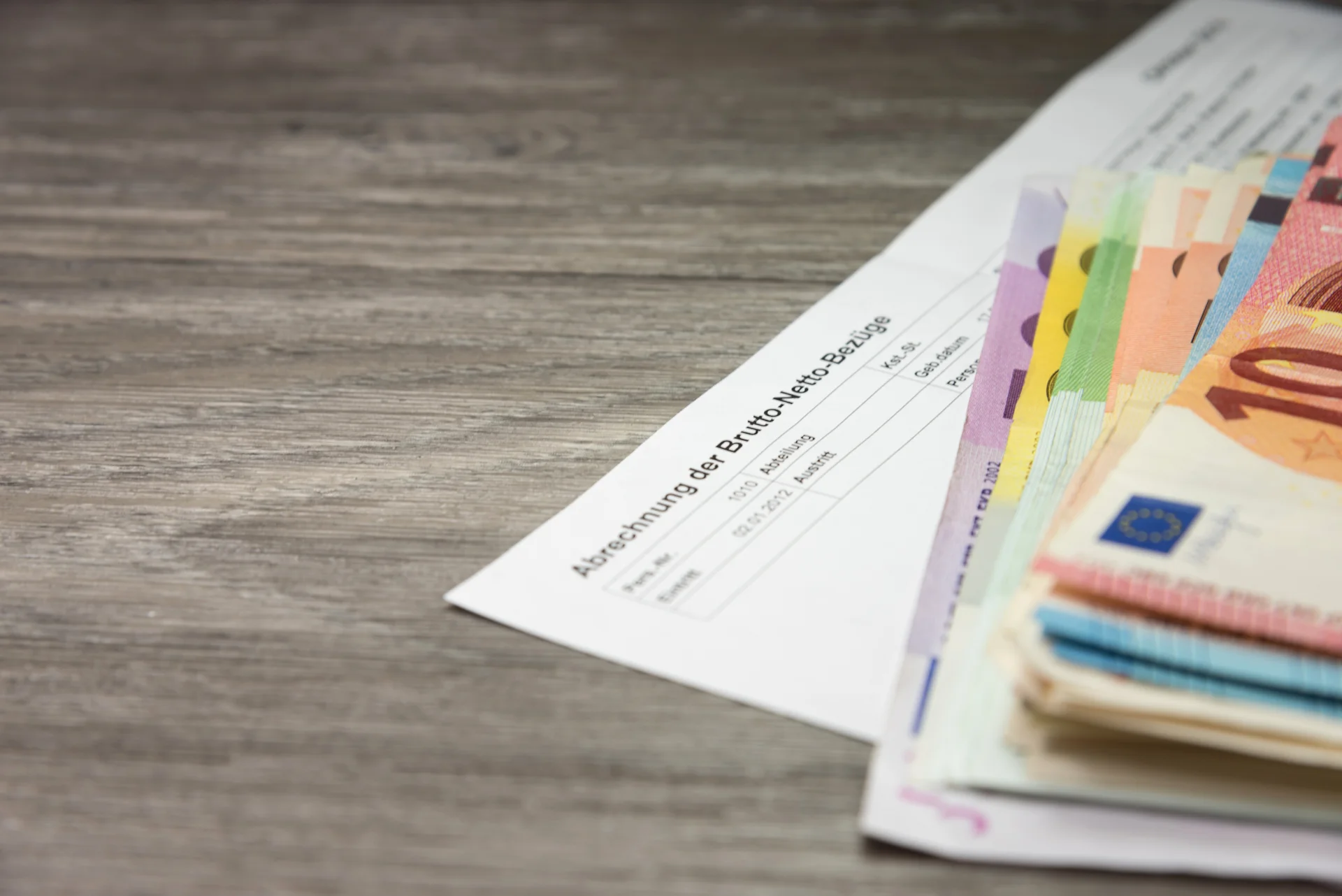 Nahaufnahme von Euro-Banknoten auf einer Lohnabrechnung mit dem Titel ‚Abrechnung der Brutto-Netto-Bezüge‘ auf einem Holztisch.